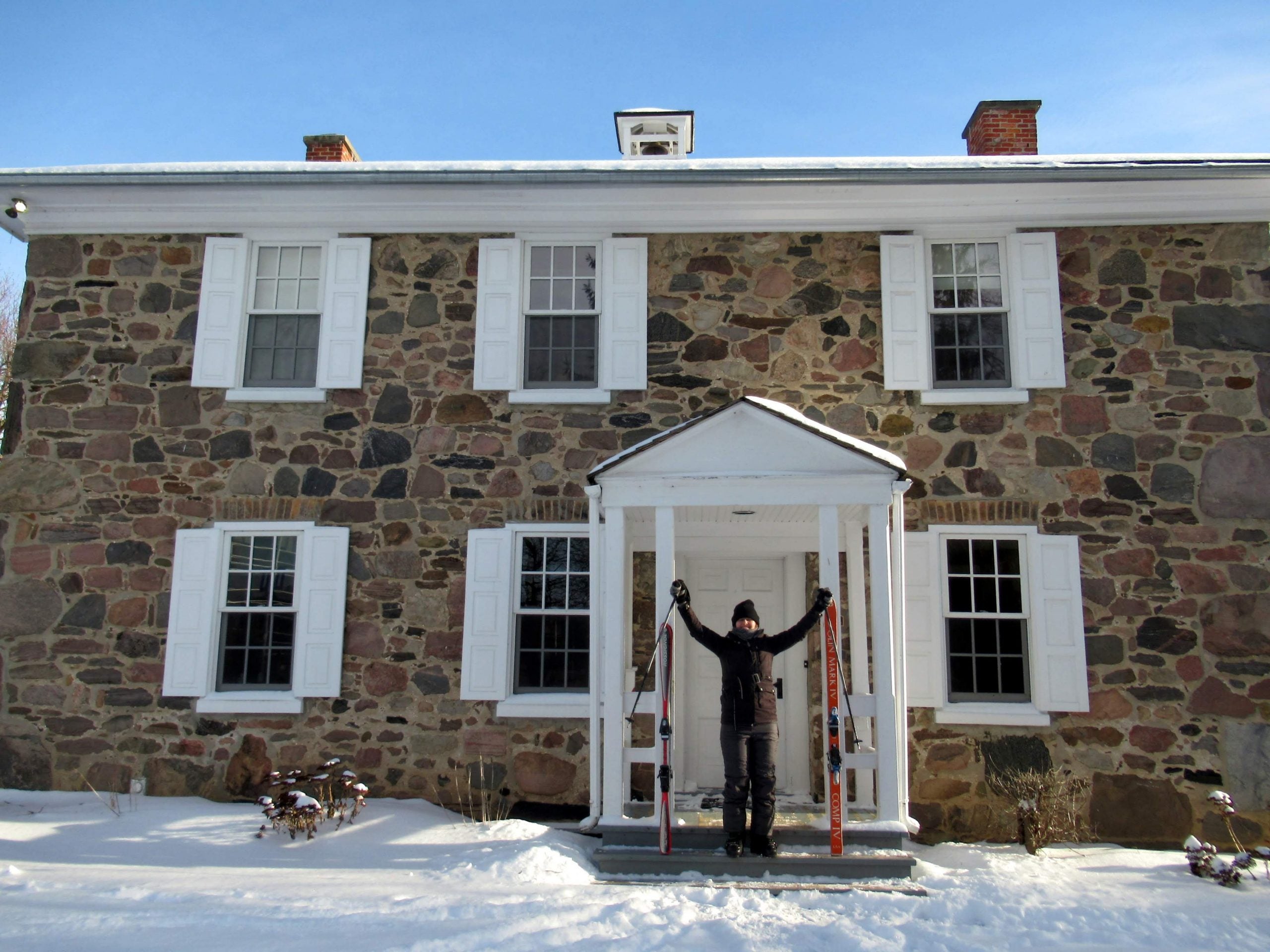 Josh holds his hands in the air on a snowy day outside Brubacher House, with cross country skis