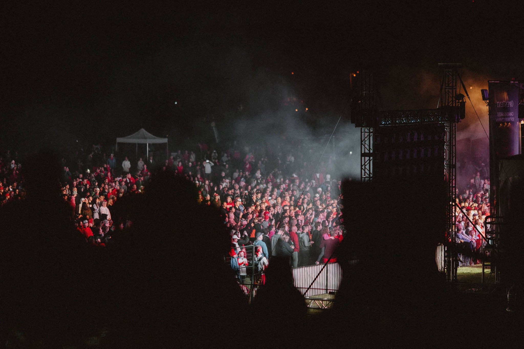 A photo of the crowd on Canada Day enjoying a concert at night, lit by the lights of the main stage.