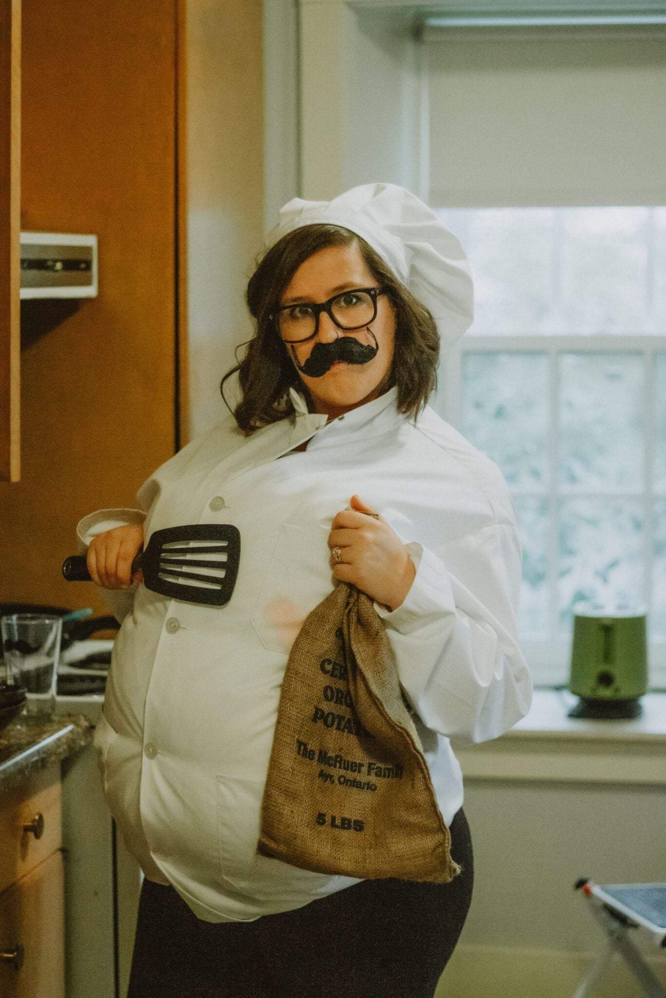 Jacquie shows off her chef costume, wearing a white shirt stuffed with pillows, a fake mustache and chef hat.