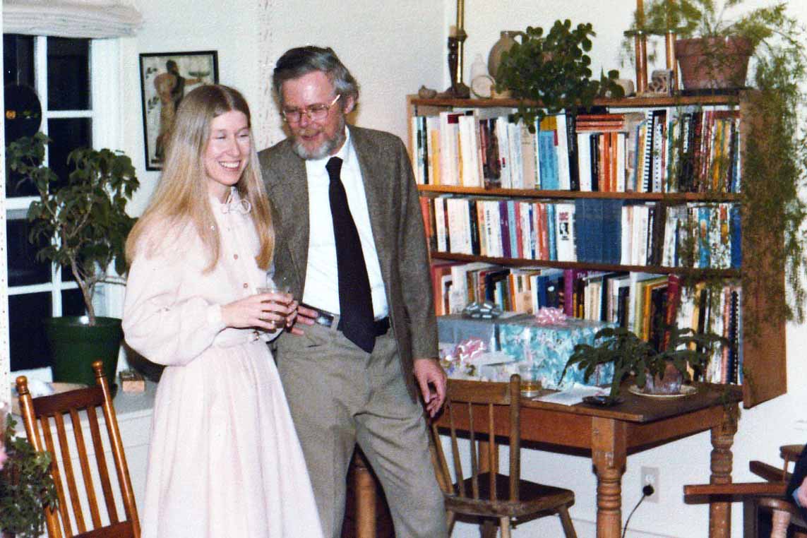 Nancy and Ted stand beside a bookshelf and desk in Brubacher House, as part of their wedding reception with family