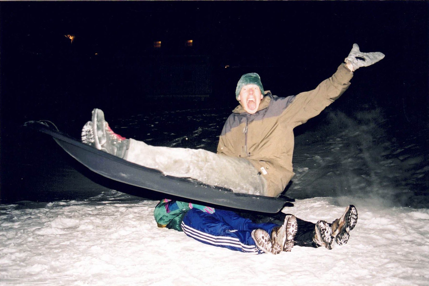 a dramatic photo of Colin in a tobbogan, mid air, above two people lying in the snow.