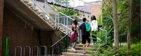 3 students standing chatting on a set of stairs in the front of Village 1