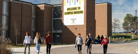 People walking in front of a large welcome to campus housing sign.