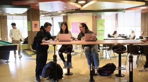3 students sitting at a high top table in REV around laptop