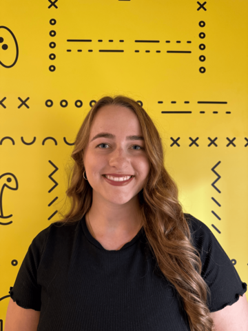 Person standing in a black t-shirt in front of a yellow banner with black UWaterloo logos. 
