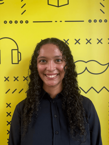 Person standing in a black long sleeve in front of a yellow banner with black branded UWaterloo logos. 