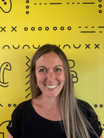 Person in a black t-shirt standing in front of a yellow banner with black branded UWaterloo logos.