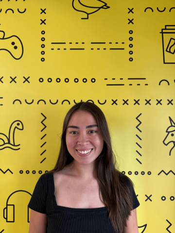 Person standing in a black t-shirt in front of a yellow banner with black UWaterloo logos. 