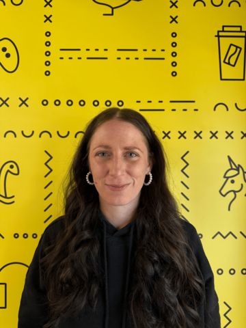 Person in a black sweater standing in front of a yellow banner with black branded UWaterloo logos.