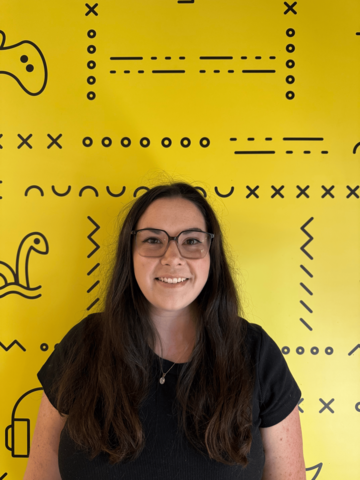 Person in a black t-shirt standing in front of a yellow banner with black UWaterloo logos. 