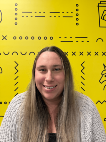 Person in a grey sweater standing in front of a yellow banner with black UWaterloo logos.