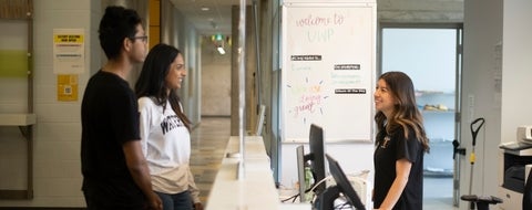 Two students being helped by a front desk assistant. 