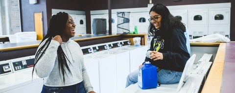 Two women going laundry and laughing.