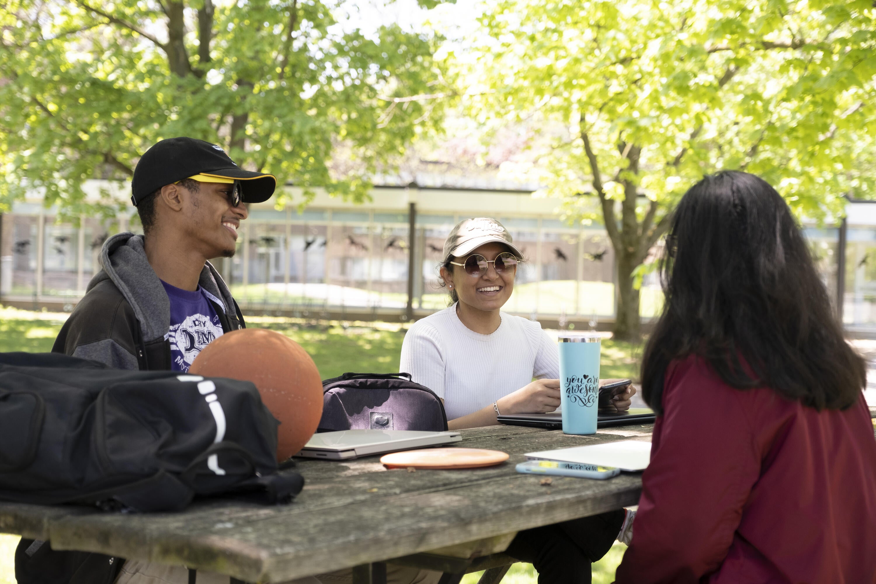 3 students sitting at a picnic table outside of REV.