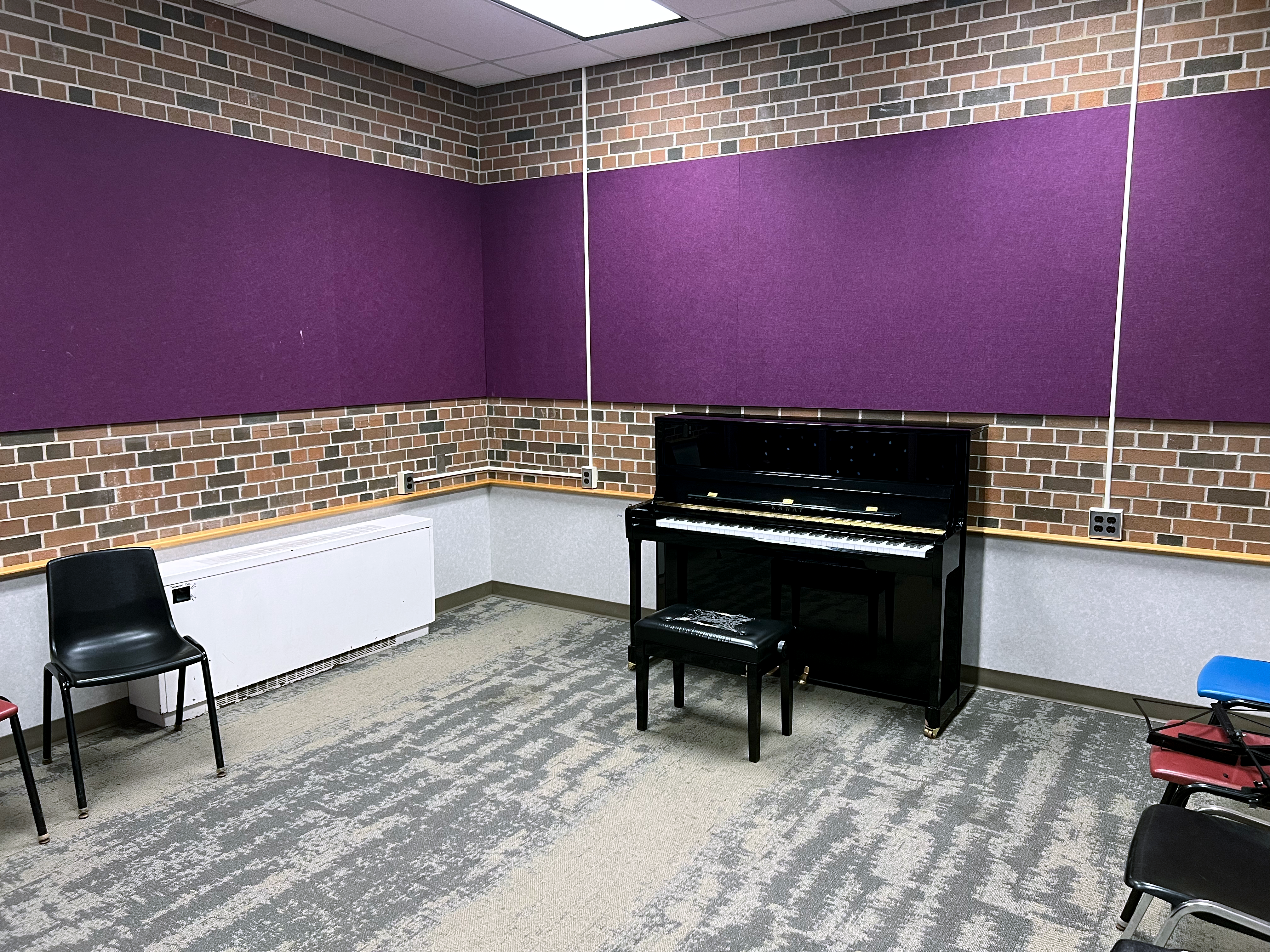 Village 1 piano room, with one grand piano, chairs around the room and purple walls.