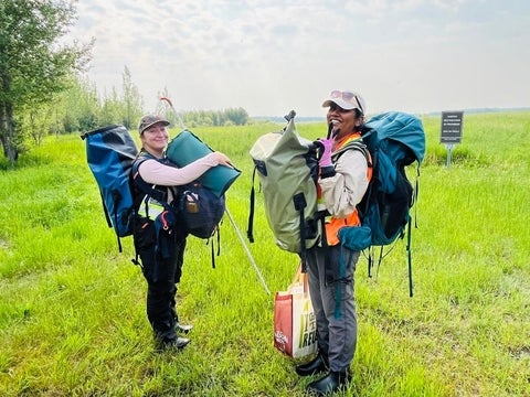 Two peatland researchers carrying heavy bags