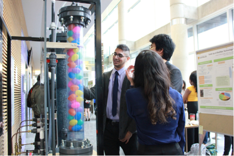 3 people looking at tall cylinder with plastic balls inside