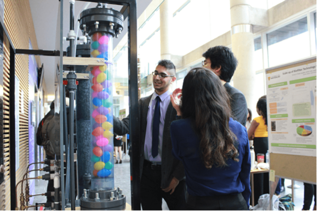 3 people looking at tall cylinder with plastic balls inside