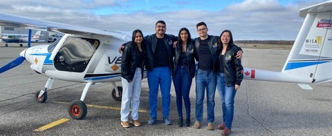 5 Students standing next to airplane