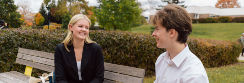 Two students seated on bench talking