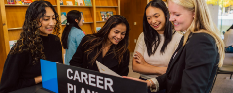 Four female students looking at a book in the career planning section of the Tatham Centre