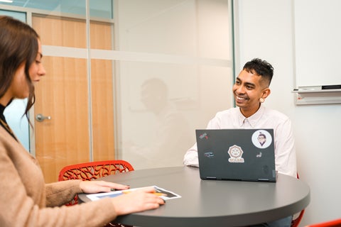 man and woman talking at a table with a laptop open