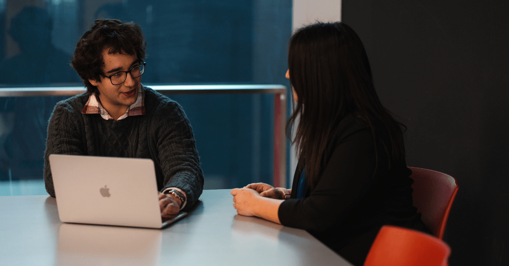 man sitting at table with laptop talking to woman