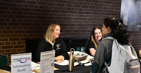 two women talking to a student wearing a backpack
