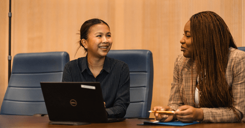 two women sitting at table with laptop open