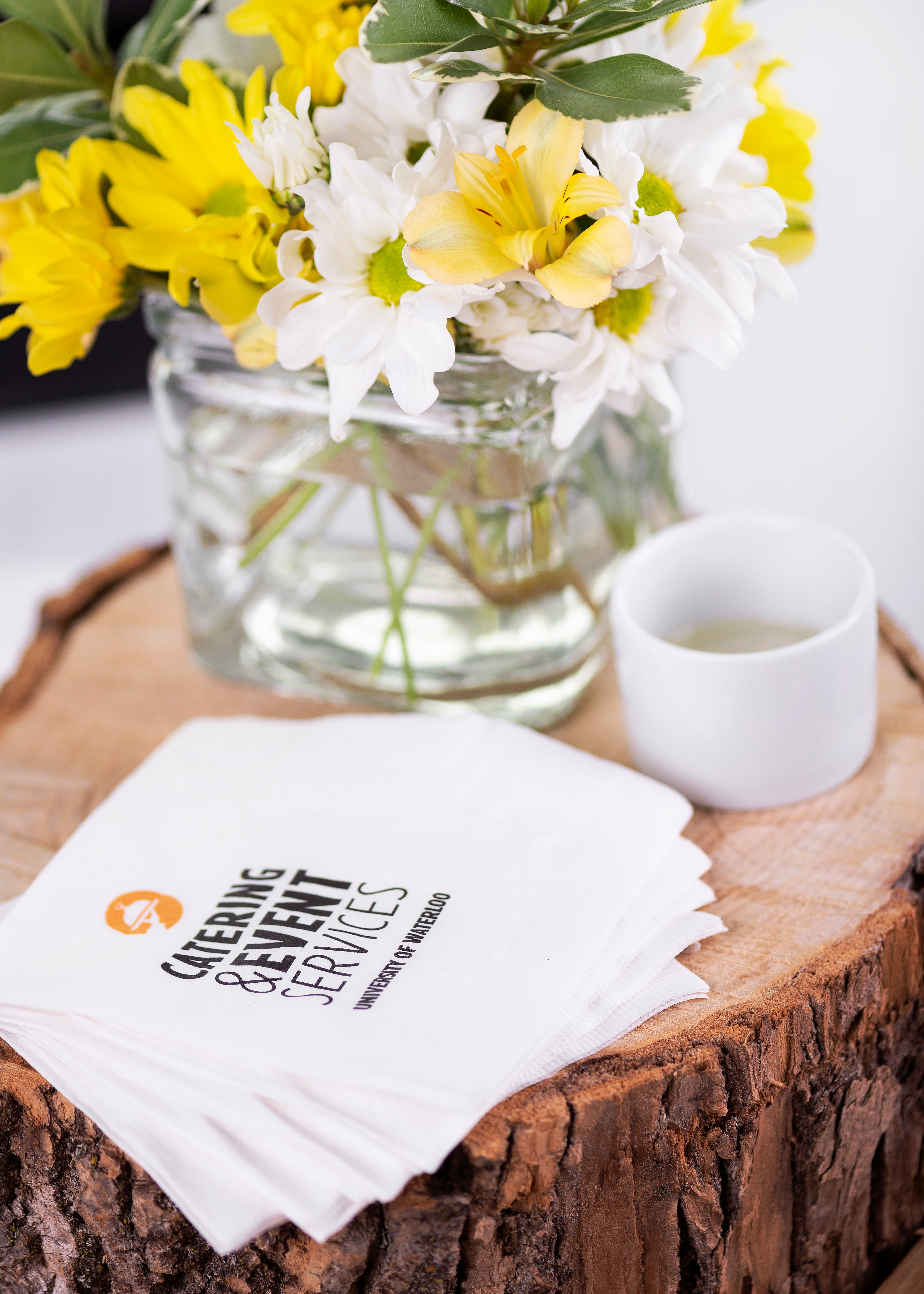 Catering branded napkins on a log with a bouquet of flowers