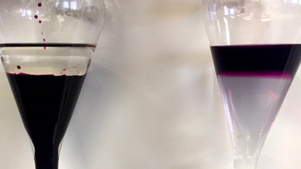 Two separatory funnels side-by-side both having two layers – clear layer atop a dark purple solution; purple layer atop clear 