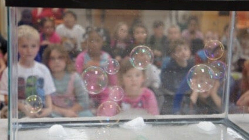 Soap bubbles floating in an empty aquarium tank with children in the background watching. 
