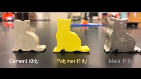 three molded cats of the same shape – one in gray cover cement, one yellow polymer and one silver metal