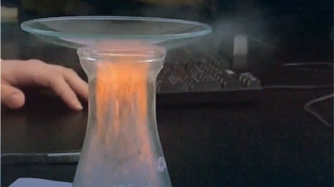 Orange flames on top of a clear solution in an Erlenmeyer flask. A watch glass on top of the flask.