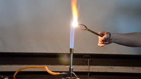 Bunsen burner and burning substance held in the flame by tongs.