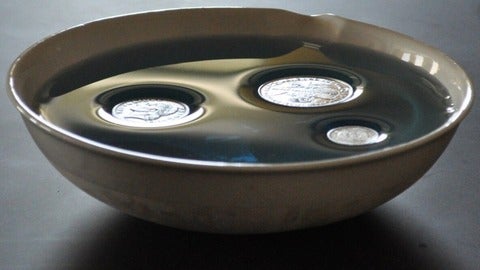 Three coins floating on water in a bowl.