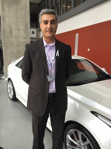 Amir Khajepour standing in front of a new white car. He is wearing a black blazer with a violet dress shirt.