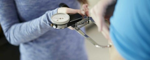 Woman using skinfold calipers as a tool to measure body fat.