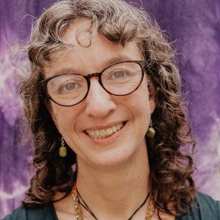 Person smiling with dark rimmed glasses and curly hair