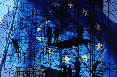 Scaffolding and men in shadow, in front of a very large EU flag