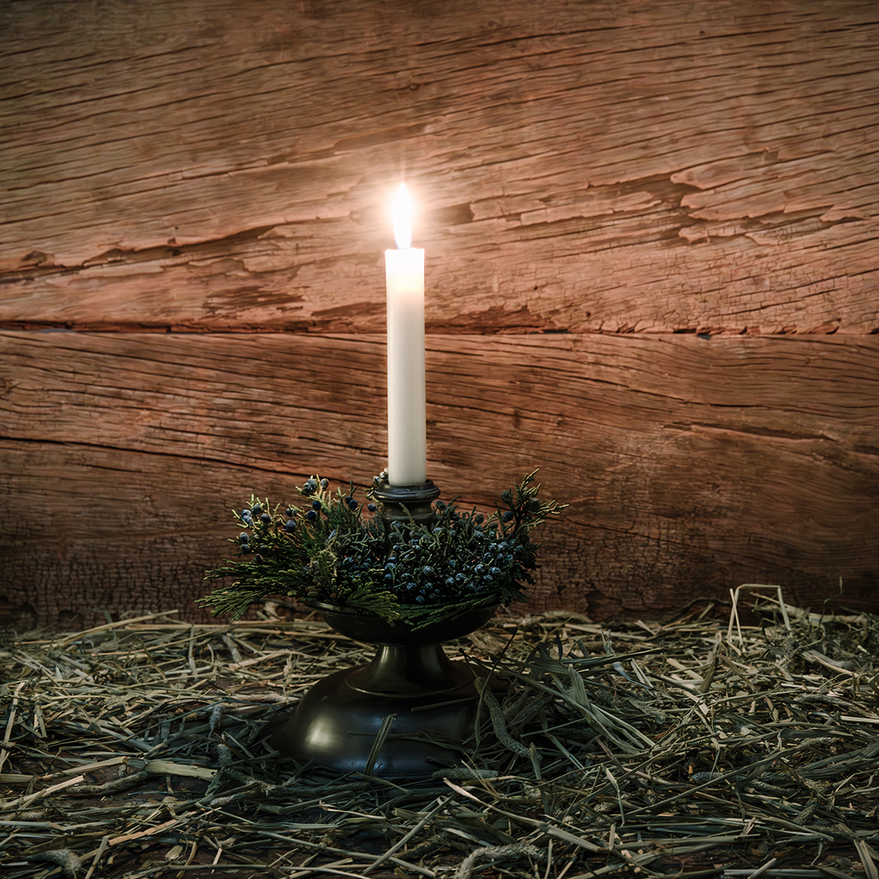 Lit advent candle on hay in front of wood.