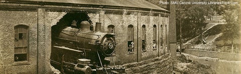 A locomotive has crashed through the back wall of a railroad roundhouse.