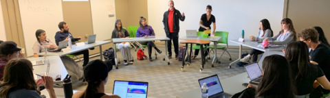 Adam Ellis addresses students seated at desks arranged in a circle