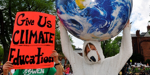 Sign reading "Give Us CLIMATE Education" on the left and person holding globe above head on right