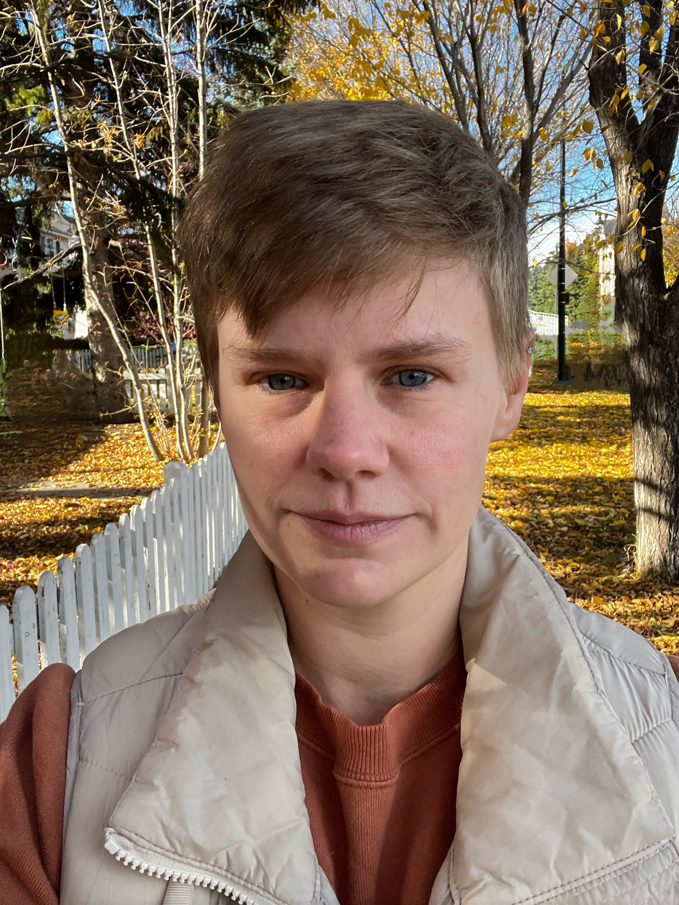 Sam Hossack, a person with short hair standing in front of Fall trees and leaves