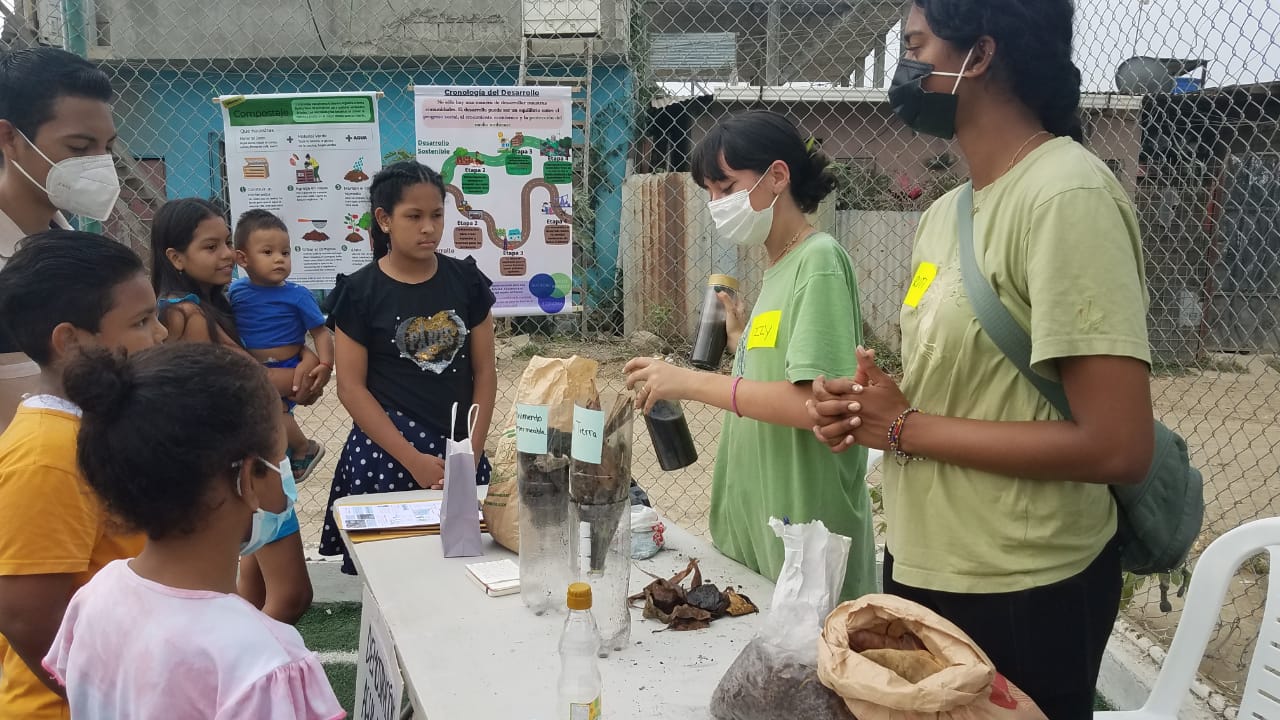 Image of two older girls in green tshirts teaching a group of children about science outdoors