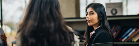 Two female students are sitting at a desk and discussing in the Tatham Centre