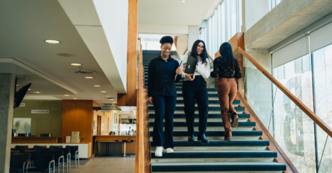 Three female students smiling and walking down the steps in Tatham Centre