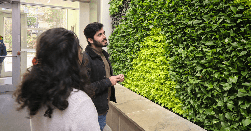 Student and faculty standing in front of plant wall