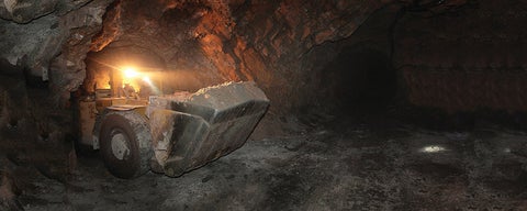 Mining construction vehicle exits underground tunnel in mine.